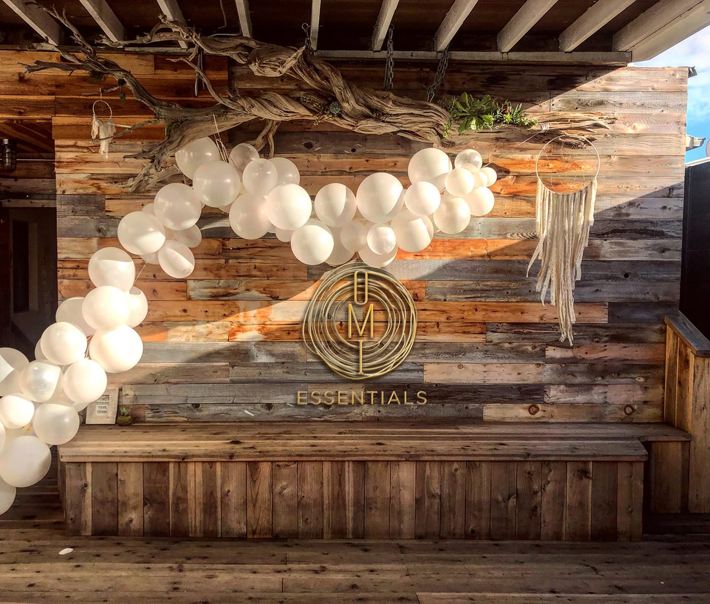 wood planked spa with dreamcatcher and white balloons and OMI Essentials logo