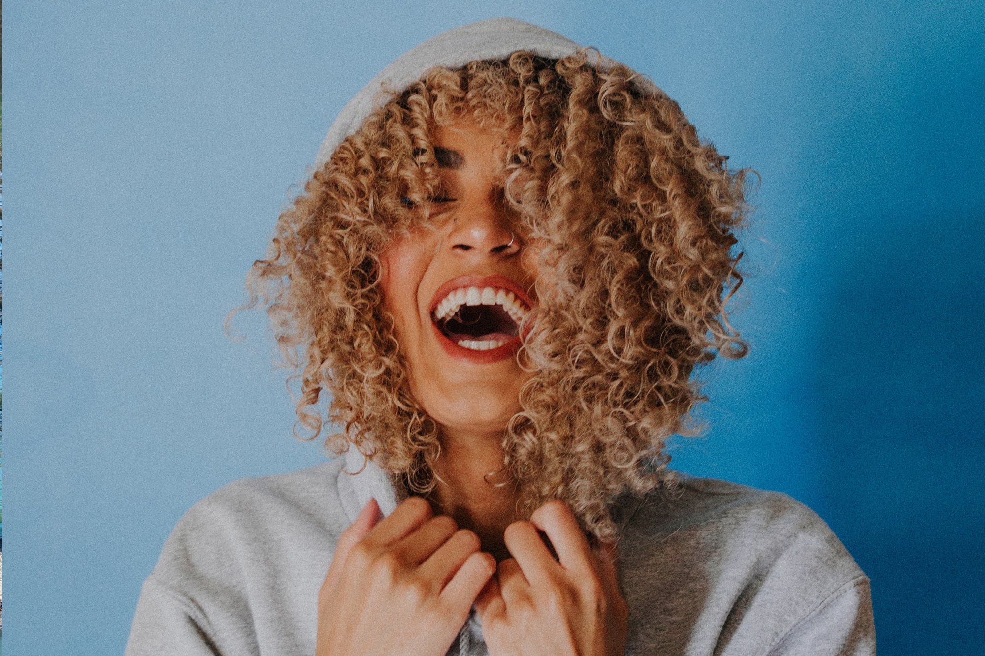 happy woman laughing wearing hoodie against blue background